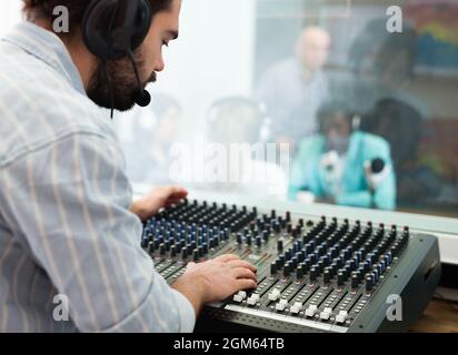 Professioneller Toningenieur, der den Tonpegel während der Live-Radiosendung mit dem Studio-Mixer reguliert Stockfoto