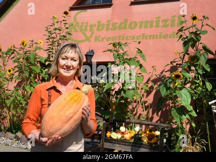 08. September 2021, Sachsen, Zwethau: Andrea Schmidt steht mit einem Halloween-Kürbis vor ihrem 'Kürbis-Domizil'-Museum. Hunderte von verschiedenen Kürbissen aus der ganzen Welt sind im Kürbismuseum zu sehen und zeigen die Vielfalt und den Einsatz von Utensilien bis hin zu Musikinstrumenten in jeder erdenklichen Form. Tausende essbarer und ornamentaler Kürbisse von rund 100 Sorten werden derzeit aus ihrer Anbauflache geerntet und können im Gartenmuseum erworben werden. Zu den drei bis 80 Zentimeter hohen oder breiten bunten oder grauen, grünen und weißen Früchten gehören der Muscat, Spaghetti oder Casperita und AC Stockfoto