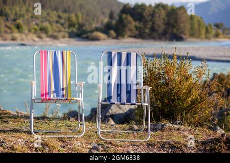 Klappstühle am Ufer eines Bergflusses an einem schönen, warmen Tag. Ein ruhiger und ruhiger Ort zum Entspannen und Nachdenken. Ausrüstung und die Erholung des Touristen. Stockfoto