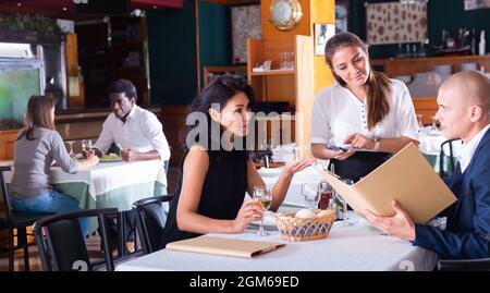 Positive weibliche Busboy nimmt Auftrag zu paar in modernen Restaurante Stockfoto