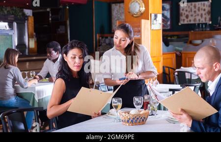 Positive weibliche Busboy nimmt Auftrag zu paar in modernen Restaurante Stockfoto