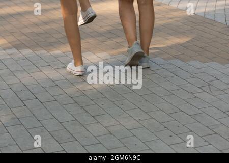 Beine von zwei jungen Frauen, die in der modernen Stadt auf Pflastersteinen laufen Stockfoto