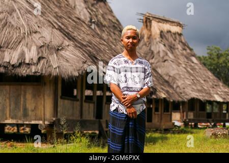 Ein junger Mann, der Sarong mit traditionellen Häusern im Hintergrund des Dorfes Wologai im Osten von Nusa Tenggara trägt Stockfoto