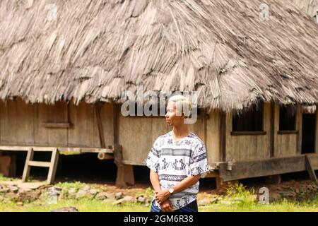 Ein junger Mann, der Sarong mit traditionellen Häusern im Hintergrund des Dorfes Wologai im Osten von Nusa Tenggara trägt Stockfoto