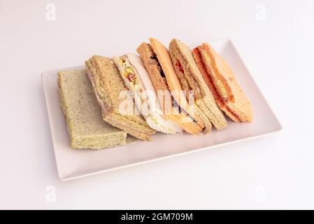 Sandwich aus verschiedenen Brotscheiben mit Füllungen zur Auswahl auf einem weißen rechteckigen Tablett und weißem Hintergrund Stockfoto