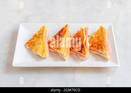 Gemischtes Sandwich aus gegrilltem, geschnittenem Brot mit Käse und Schinken auf einem weißen Teller. Stockfoto