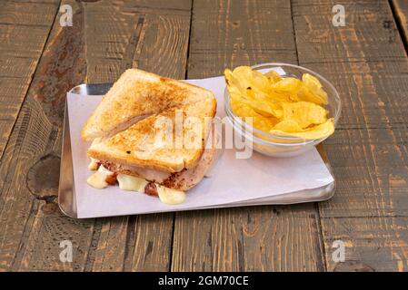 Gemischtes Sandwich mit geröstetem, in Scheiben geschnittenem Brot, gegrilltem Schinken und geschmolzenem Käse, der mit gebratenen Kartoffeln am Rand tropft. Stockfoto