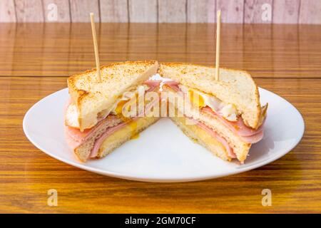 Doppeldecker-Sandwich zum Frühstück oder ein Snack mit einem Spiegelei, mehreren Schinkenscheiben und geschmolzenem Käse und dem in Scheiben geschnittenen Brot ging durch den Grill Stockfoto