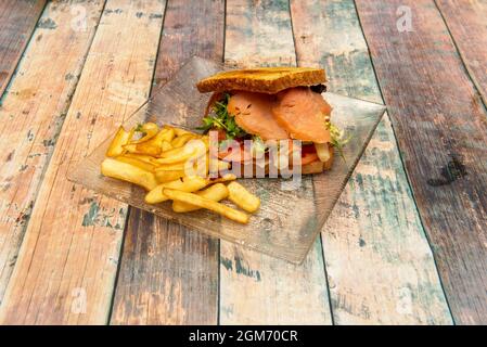 Norwegisches Sandwich mit geräuchertem Lachs, weißem Spargel, Tomatenscheiben, Käse und Escarole, garniert mit Pommes frites Stockfoto