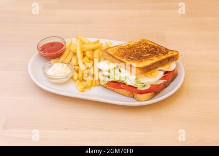 Super-Gemüse-Sandwich mit gekochtem Ei, gehackten Tomaten, Eisbergsalat und einer Seite Pommes auf einem weißen Porzellanteller Stockfoto