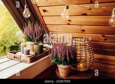 Kleiner natürlicher Holzbalkon mit Heideblumen, Kerzenlicht-Flamme und dampfender Tasse Tee. Niedliche Herbst Hygge Home Dekor arrangem Stockfoto