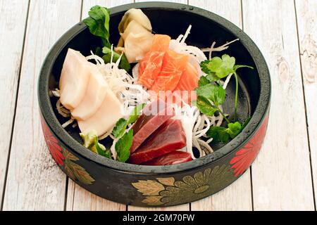 Schwarzes Tablett im asiatischen Stil mit Blumenmuster, gefüllt mit norwegischem Lachs-Sashimi-Sushi-Tacos, rotem Thunfisch, Butterfisch und Reisnudeln mit frischer Petersilie Stockfoto