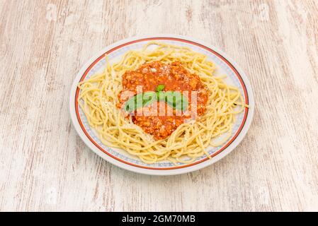 Typische und super einfache Teller mit Spaghetti mit Bolognese-Sauce, mit geriebenem Käse und Basilikum auf einem hellen Holztisch Stockfoto