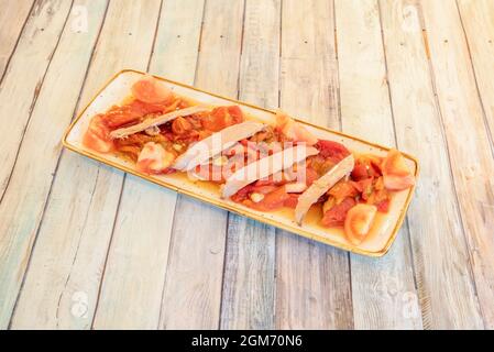 Thunfisch-Bauchsalat mit roten Paprika und Tomaten auf langem Teller auf farbigem Plankentisch Stockfoto