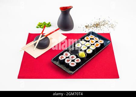 Schwarzes Tablett mit achtzehn reifen Avocado Maki, norwegischem Lachs, Nori-Algen, rotem Thun, edamamen Bohnen, Essstäbchen und Schüssel mit Sojasauce und Wasabi Stockfoto