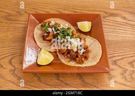 Zwei mexikanische Tacos mit Weizentortillas, gefüllt mit Osso Buco birria mit Kalkstücken, die auf einem Tonteller garniert werden können Stockfoto