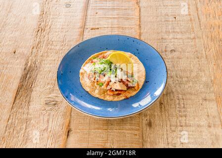 Köstliche Carnitas mexikanischer Taco mit Koriander, geschmortes Fleisch, mit roher Zwiebel und Zitronenkeil mit Weizentortilla und blauer Avocado auf schönem hellem Holz Stockfoto