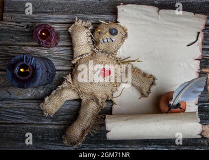 Klassische mystische Voodoo-Puppe aus Sackleinen für die Durchführung eines magischen Rituals auf einem rauen Holztisch im Licht brennender schwarzer Kerzen Stockfoto