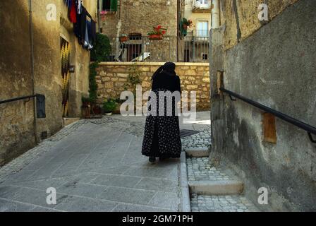 Eine ältere Frau in charakteristischem Kleid geht langsam durch die Straßen des Dorfes. Scanno, Abruzzen, Italien. Stockfoto