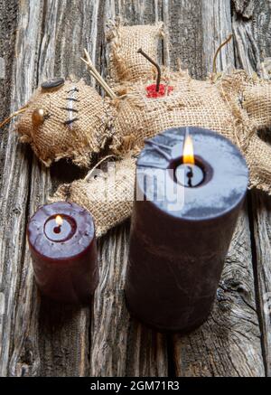 Klassische mystische Voodoo-Puppe aus Sackleinen für die Durchführung eines magischen Rituals auf einem rauen Holztisch im Licht brennender schwarzer Kerzen Stockfoto