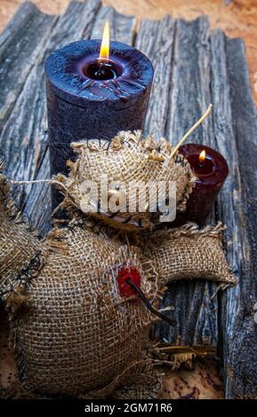 Klassische mystische Voodoo-Puppe aus Sackleinen für die Durchführung eines magischen Rituals auf einem rauen Holztisch im Licht brennender schwarzer Kerzen Stockfoto