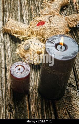 Klassische mystische Voodoo-Puppe aus Sackleinen für die Durchführung eines magischen Rituals auf einem rauen Holztisch im Licht brennender schwarzer Kerzen Stockfoto