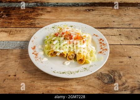 Teller mit mexikanischen goldenen Tacos mit Salat und Salsa darauf Stockfoto