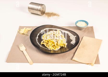 Schönes Nudelgericht mit köstlichem Tagliatelle tartufata Rezept mit geriebenem Käse und Parmesan-Flocken auf einem weißen Tisch. Stockfoto