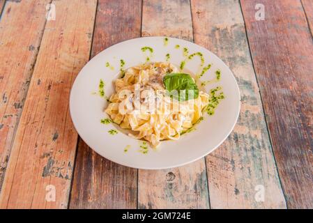 Tagliatelle funghi mit Petersiliensauce und Basilikumblättern auf weißem Teller und Holztisch Stockfoto