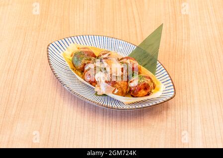 Holzschale und Bananenblatt mit Stücken japanischer Krake Takoyaki mit Scheiben getrockneten Thunfisch Stockfoto