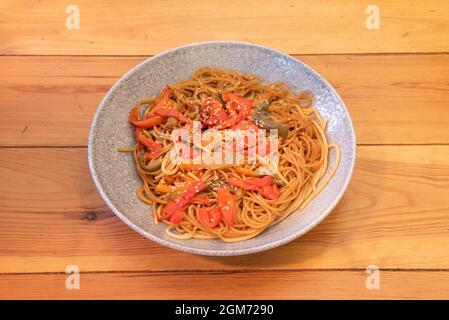 Tagliatelle in Teriyaki-Sauce mit viel roten und grünen Paprika und Sesamsamen auf dunkelgrauem Teller und Holztisch anbraten Stockfoto