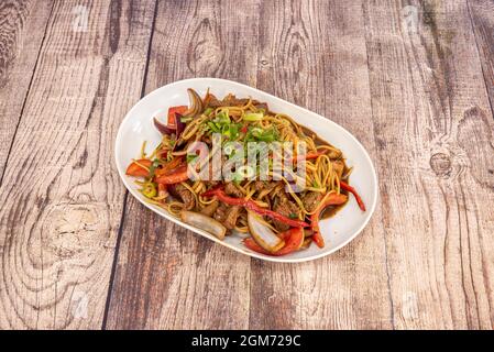 Peruanisch angebratene Nudeln mit Filetstreifen, Zwiebelstücken, Tomaten, rotem Pfeffer und grünem Schnittlauch mit Sojasauce. Stockfoto