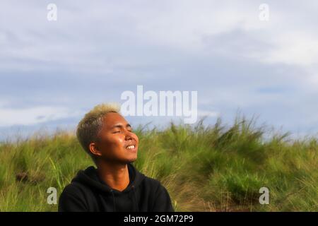 Junger asiatischer Mann mit blonden Haaren am Flughafen, der auf sein Flugzeug wartet Stockfoto