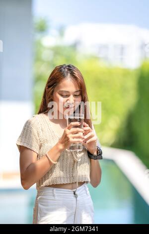 Asiatische Frau hält ein Glas Wasser aus dem Trinken auf Outdoor-Feld mit Bokeh grünen Banner Hintergrund. Stockfoto