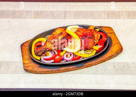 Großes und farbenfrohes indisches Tandoori-Hühnerrezept mit Zwiebeln, Paprika und Kirschtomaten auf einem Metalltablett Stockfoto