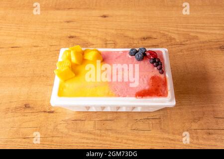 Eine Kilo Eiscreme mit roten Früchten und die andere Hälfte mit Mango auf einem Holztisch Stockfoto
