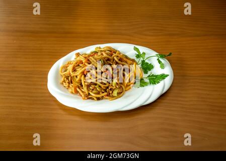 Asiatische udon-Nudeln mit heißer Sauce, sautiertem Obst, Gemüse und Karotten sowie Hühnerfleisch mit Petersilie auf weißem Tablett Stockfoto