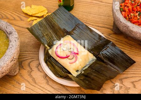 Mexikanisches Tamale mit Rezept für Cochinita pibil auf gefaltetem Bananenblatt. Pico de gallo und Tortilla Chips Stockfoto