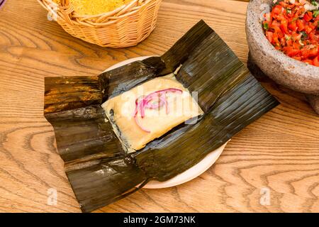 Mexikanische Tamale von Cochinita pibil in Maiskolben Blatt mit vulkanischem Stein molcajete gefüllt mit Pico de gallo geschmort Stockfoto