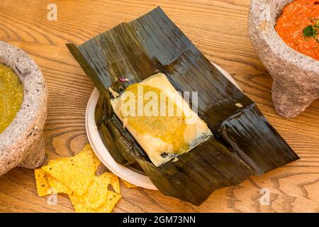 Beliebte mexikanische Chicken Tamale in grüner Sauce auf Bananenblatt, mit Mais Nachos und Vulkangestein Molcajetes Stockfoto