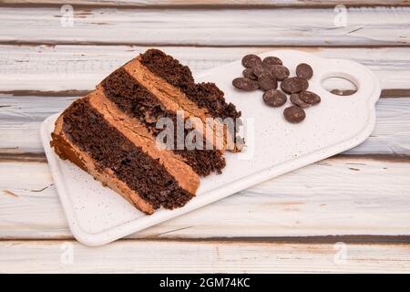 Portion Schokoladenkuchen mit drei Schichten Kekse und Füllung mit Schokoladensplittern auf einer Seite auf weißem Tisch Stockfoto