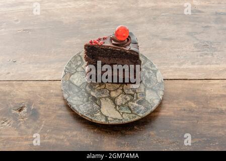 Schokoladenkuchen mit drei Schichten Biskuitkuchen und zwei Schichten Füllung mit einer kandierten Kirsche darauf Stockfoto