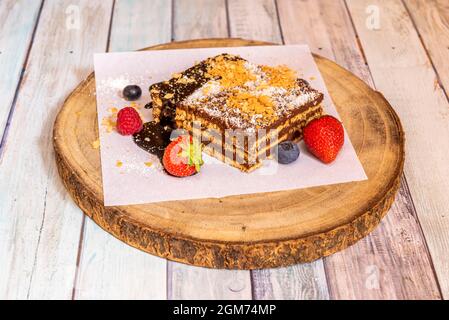 Köstliche und farbenfrohe Portion Großmutter's Cake mit drei Schichten Schokolade und drei Schichten Keks, geriebener Kokosnuss auf der Oberseite und Beeren auf Stockfoto