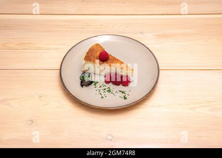 Portion hausgemachter Käsekuchen mit Himbeeren auf Holztisch Stockfoto