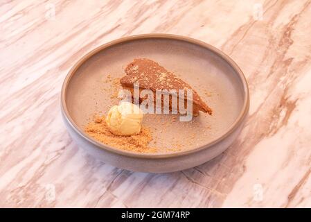 Portion Käsekuchen und Dulce de leche mit einer Kugel Vanilleeis mit gemahlenem Keks Stockfoto