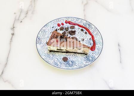 oreo-Kuchen mit Schokoladenstückchen und rotem Fruchtsirup auf weißem Marmortisch Stockfoto