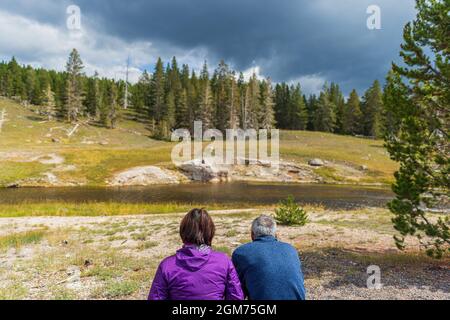 Paar warten auf den Ausbruch des Riverside Geyser im Old Faithful Basin, Yellowstone National Park Stockfoto