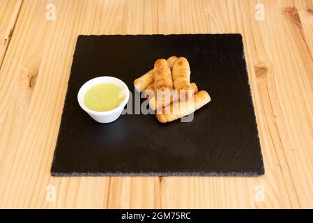 Anteil venezolanischer tequeños gefüllt mit Queso Fresko und Avocado-Sauce zum Eintauchen auf einen schwarzen Schieferteller Stockfoto