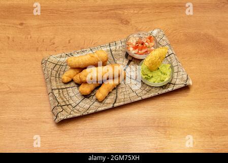 Ähnliche Holzplatte mit einer Portion tequeños gefüllt mit frischem Käse garniert mit Guacamole und Pico de gallo Stockfoto