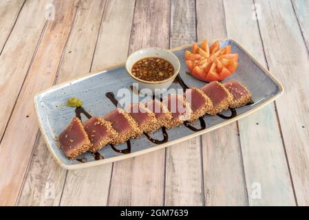 Köstliches rotes Thunfisch-Tataki mit Samen und Sauce zum Eintauchen auf einen blauen Teller Stockfoto